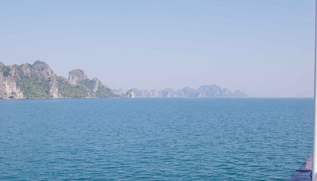 Passengers on board boat look out at the mountainous islands of Halong bay