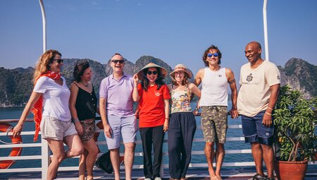 Passengers on board boat in Halong bay pose for camera with mountains behind them