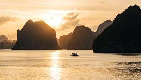 A small fishing boat crosses the waters of Ha Long Bay at sunset