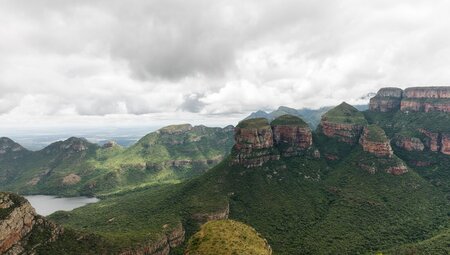 Large round stone spires seperate from a larger plateau covered in green trees rise up from a huge canyon