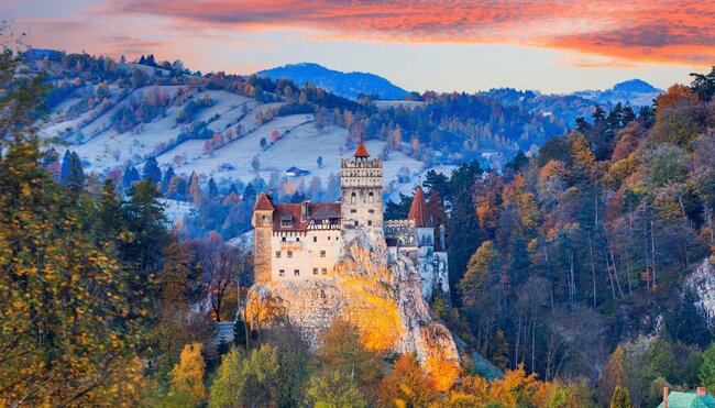 Wide view of medieval Bran Castle during sunset with warm autumn colours of surrounding trees, Transylvania, Romania