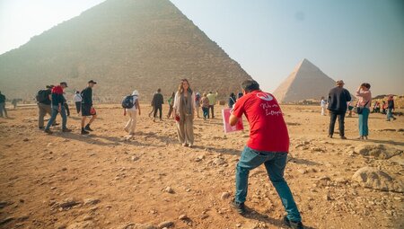 Leader takes a photo of a traveller posing in front of the Pyramids of Giza, Egypt