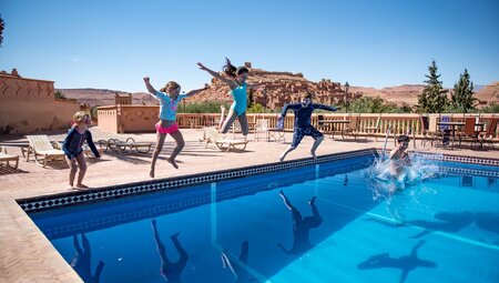 Group of Intrepid traveller children jumping into a pool with the kasbah of Ait Benhaddou in the background