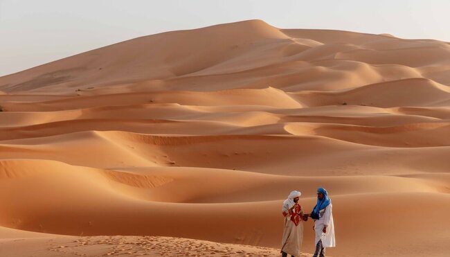 Local guides in the Sahara Desert, with vast sand dune landscape behind them, Morocco