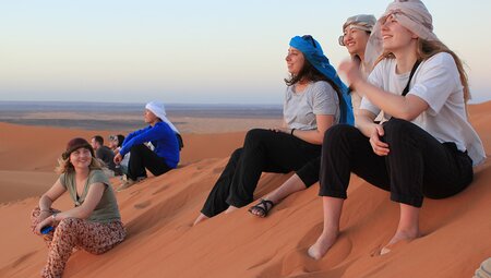 Group of travellers watching the sunset in the Sahara desert in Morocco