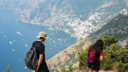 Two travellers hiking on the Path Of The Gods with a great view of the boats and village on Amalfi Coast