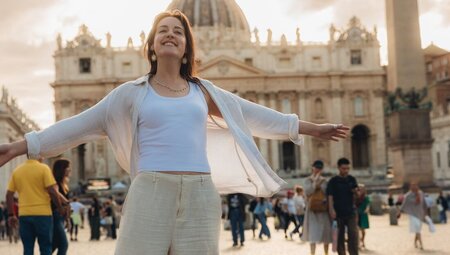 Smiling traveller posing in St. Peter's Square with  St. Peter's Basilica in the background during sunset, Vatican Square, Italy