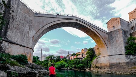 Intrepid traveller looks up from riverbed at the majesty of an ancient Ottoman bridge in Mostar Bosnia and Herzegovina