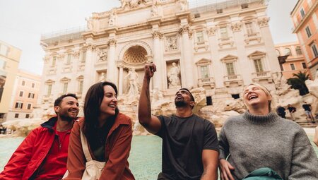 Travellers smiling as one flicks coin into the Trevi Fountain, Rome, Italy