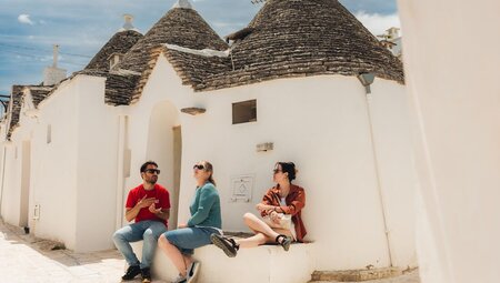 Travellers sitting on ledge outside traditional trulli buildings in Alberobello, Italy