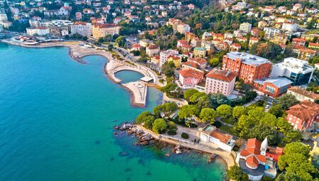An aerial drone view of the coastal town Opatija in Croatia, showing rooftops and treetops