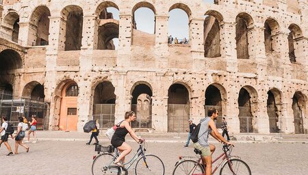 Two travellers cycle past the Colosseum in Rome