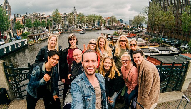 Group of travellers pose for a selfie smiling on a canal bridge in Amsterdam