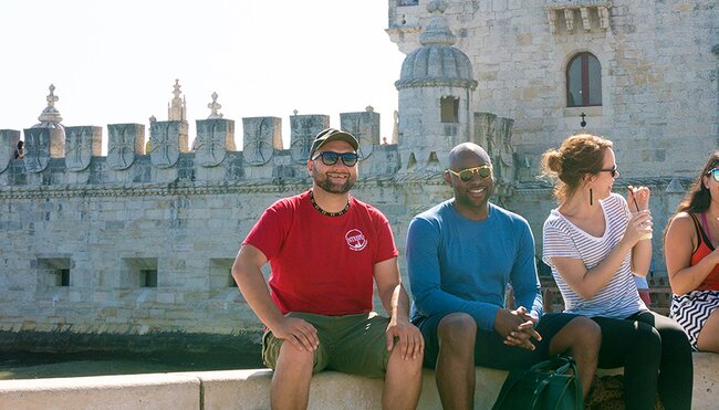 Intrepid Travel group sitting on river bank in front of Belem Tower, Lisbon, Portugal