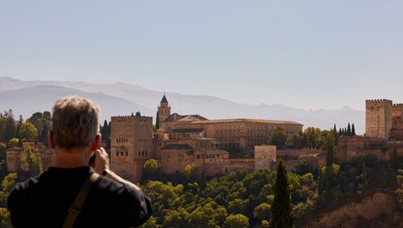 Alhambra Fortress with mountains in the background and traveller taking a photo of the view in the foreground, Granada, Spain