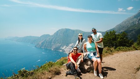 Travellers take a photo with Leader on a cliffside trail overlooking the blue sea and mountains of the Amalfi Coast, Italy