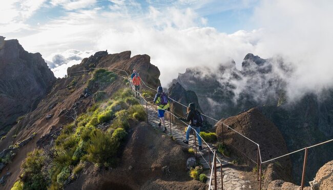 Travellers hike a narrow mountaintop path on the way to Pico do Ruivo in the sunlight of Madeira, Portugal