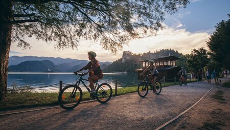 A group of cyclists riding their bikes around the stunning Lake Bled at dusk in Slovenia