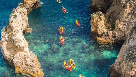 Aerial view of string of travellers in double kayaks between pale protruding cliffs near Lagos in Portugal