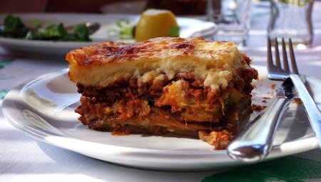 A plate of a traditional Greek dish called Moussaka on a rustic outdoor table