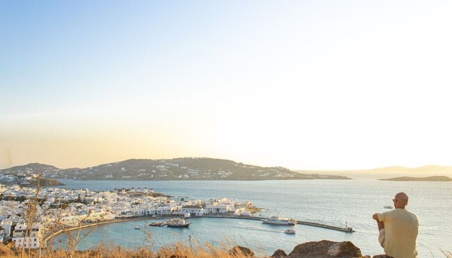 Traveller perched on a high hill looks out over the sparkling Aegean and the island of Mykonos