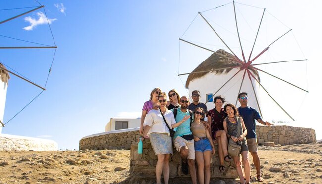Travellers pose for a group shot with the iconic windmills of Mykonos in the Cyclades