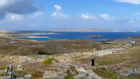 Intrepid traveller at the peak of a hike looking out over Delos and its ruins in the Cyclades