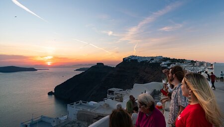 Intrepid travellers and leader look out at sunset over the Aegean Sea from a Santorini balcony