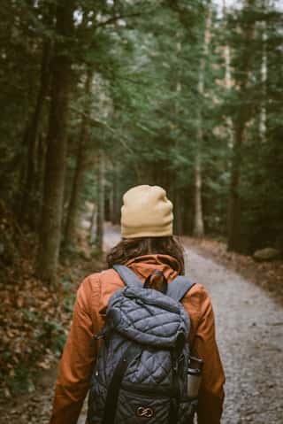Person mit Rucksack auf einem Waldweg, umgeben von Bäumen.