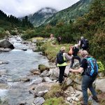 Gruppe von Wanderer ausgerüstet mit gutem Schuhwerk, Rucksack und Trekkingstöcken gehen dem Fluss entlang in ein Tal