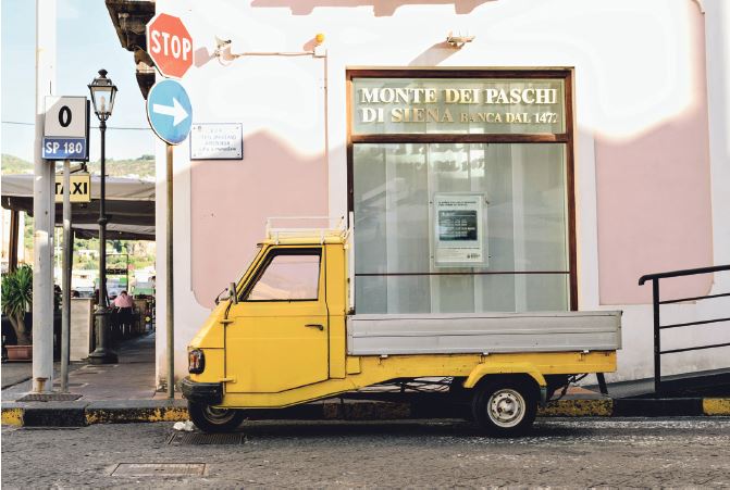 Kleines Straßenfahrzeug in Lipari Kleines gelbes Kraftfahrzeug vor einem rosaroten Gebäude.