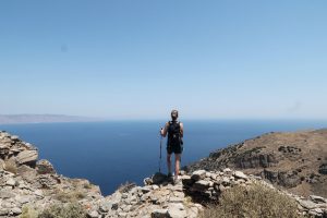 Wanderin steht auf Felsvorsprung über dem tiefblauen Meer, blauer Himmel