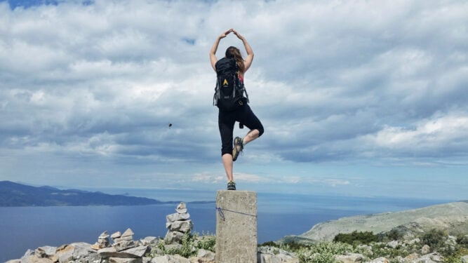 Frau in Yogahaltung auf einem Steinpflock auf einem Berg