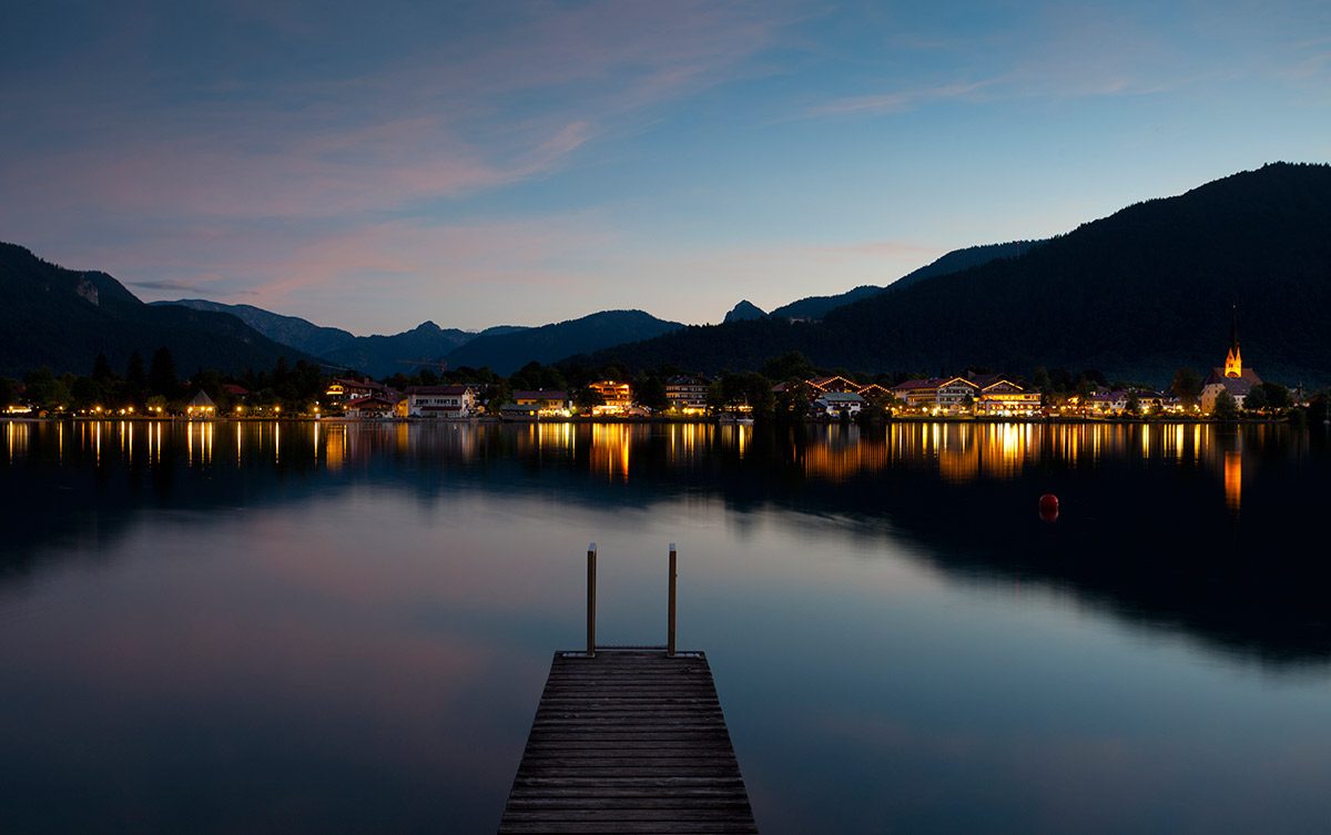 Abendstimmung am Tegernsee Ein See mit beleuchteten Häusern im Hintergrund bei Nacht
