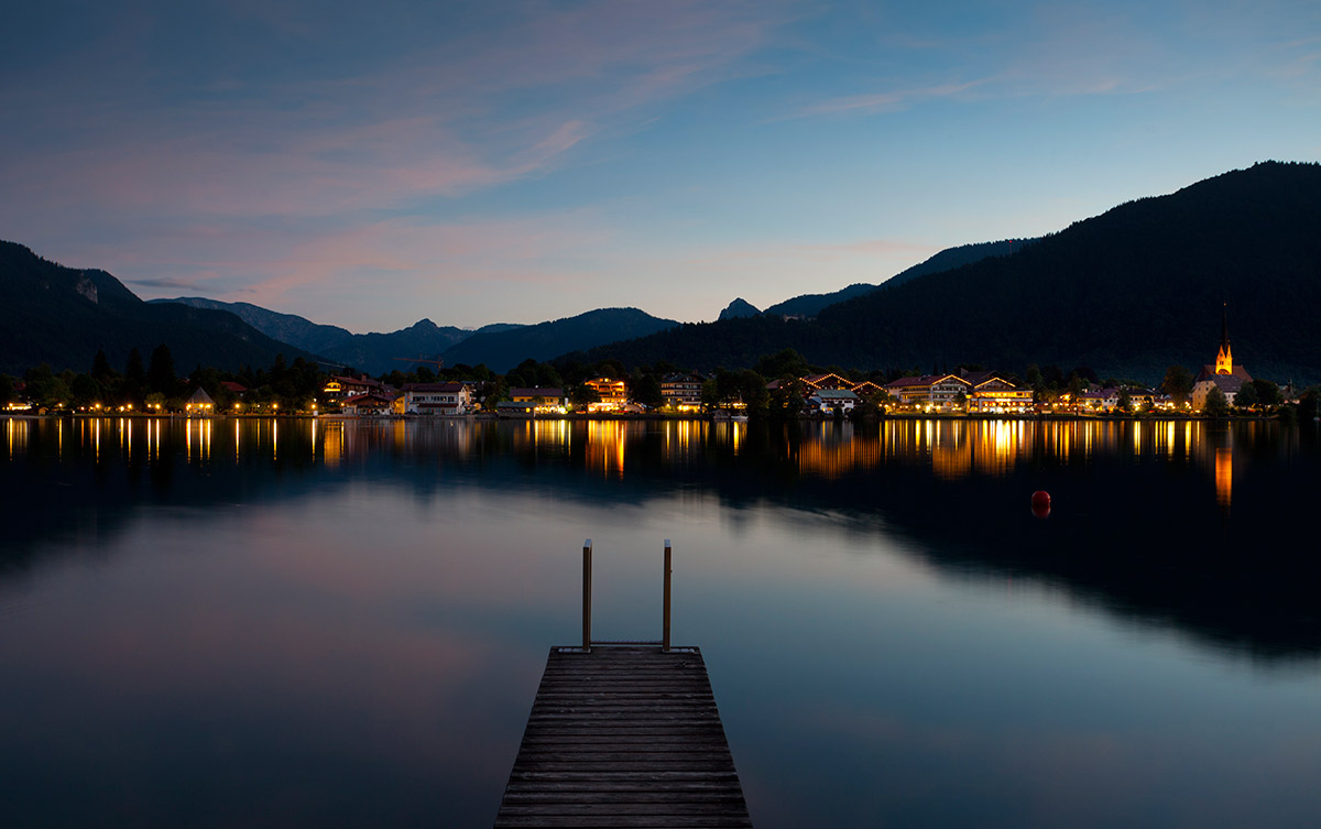 Abendstimmung am Tegernsee Ein See mit beleuchteten Häusern im Hintergrund bei Nacht