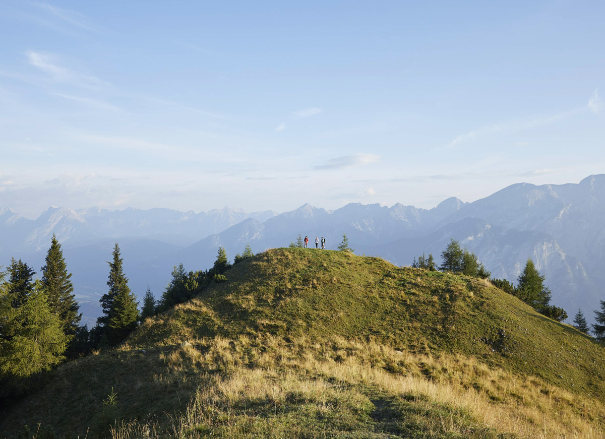 grüner hügel, drei menschen aus der ferne, berge im hintergrund