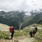 Mehrere Wanderer auf einem Pfad in den Alpen, wolkenverhangener Himmel
