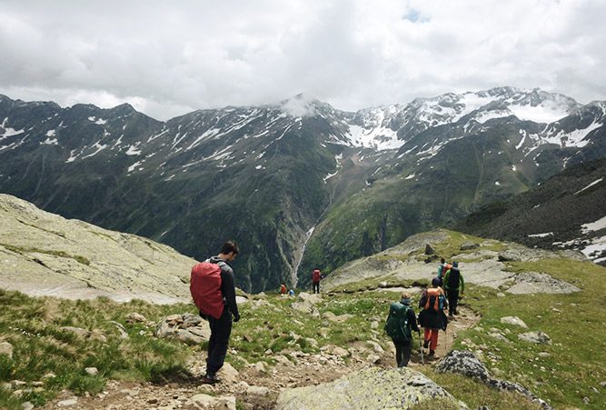 Mehrere Wanderer auf einem Pfad in den Alpen, wolkenverhangener Himmel