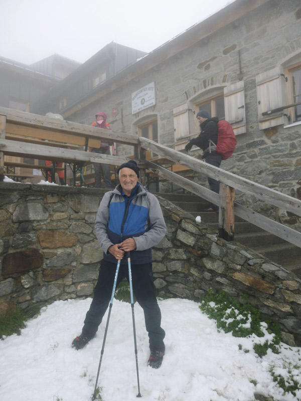 Mann mit Trekkingausrüstung vor Hütte, nebelig