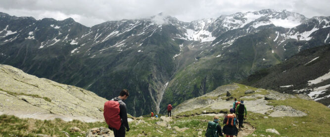 Mehrere Wanderer auf einem Pfad in den Alpen, wolkenverhangener Himmel