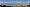 Panoramabild einer Bergkulisse unter blauem Himmel. Vor den Bergen liegt ein See.