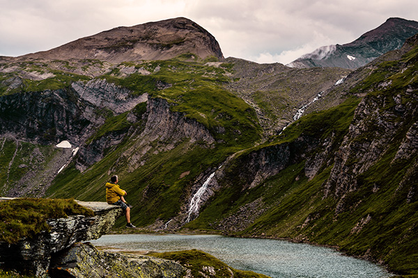 Mann auf Felsvorsprung vor einer Bergkulisse