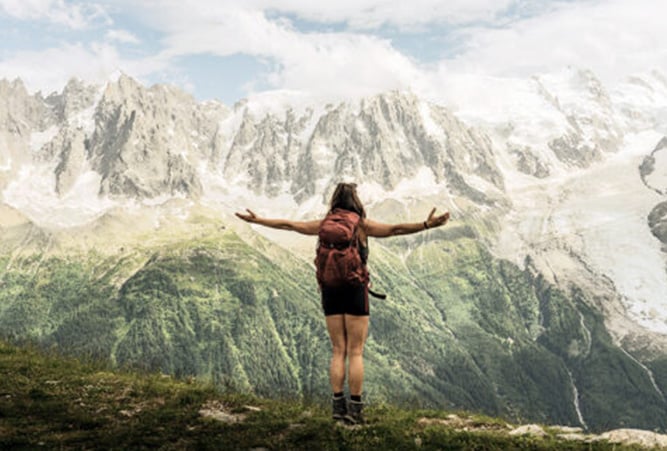 Wanderin mit ausgebreiteten Armen vor Bergkulisse in den Alpen