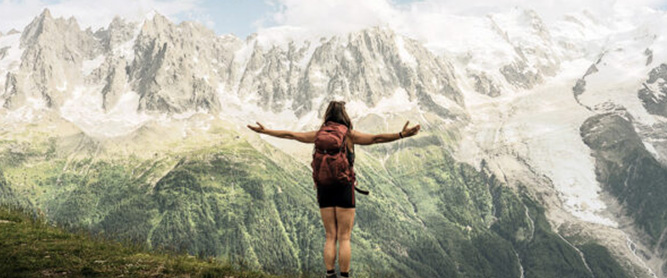 Wanderin mit ausgebreiteten Armen vor Bergkulisse in den Alpen