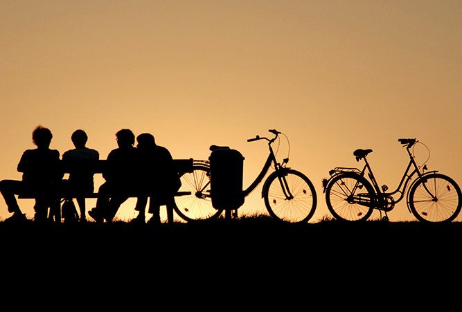 Vier Personen sitzen auf einer Bank neben ihren Fahrrädern, Abendsonne