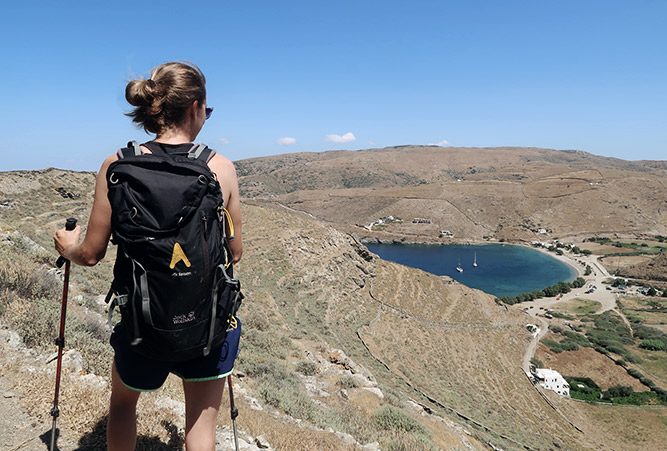 Wanderin von hinten, blickt hinunter auf einen See. Hügeliges Gelände