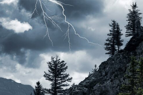 Blitz am dunklen wolkenverhangenen Himmel über Bergen mit Bäumen
