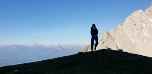 Eine Person auf einer ANhöhe, blauer Himmel im Hintergrund und letzte Sonnenstrahlen auf Bergen