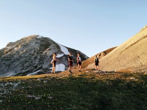 Vier Personen auf einer Wiesenfläche, goldene Sonnenstrahlen und kleine Schneefelder im Hintergrund