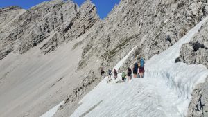 Sieben Personen an einem steilen Felshang gehen über ein Schneefeld